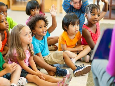 Children sit in a circle on the floor hearing a book read to them.